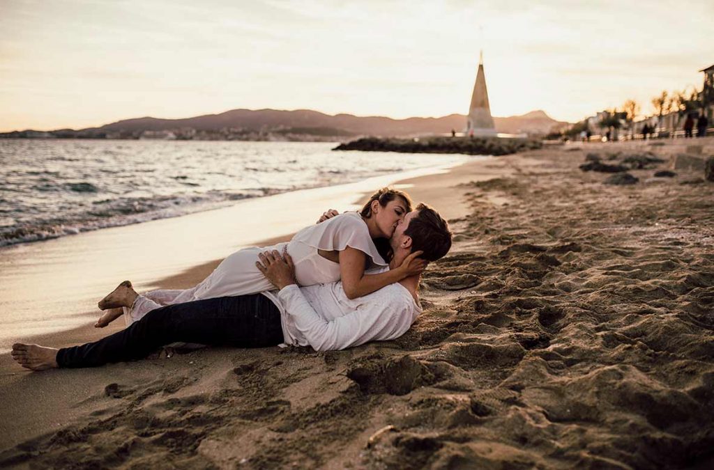 Pareja besándose tumbada en la arena durante una sesión de fotos romántica en la playa de Mallorca al atardecer