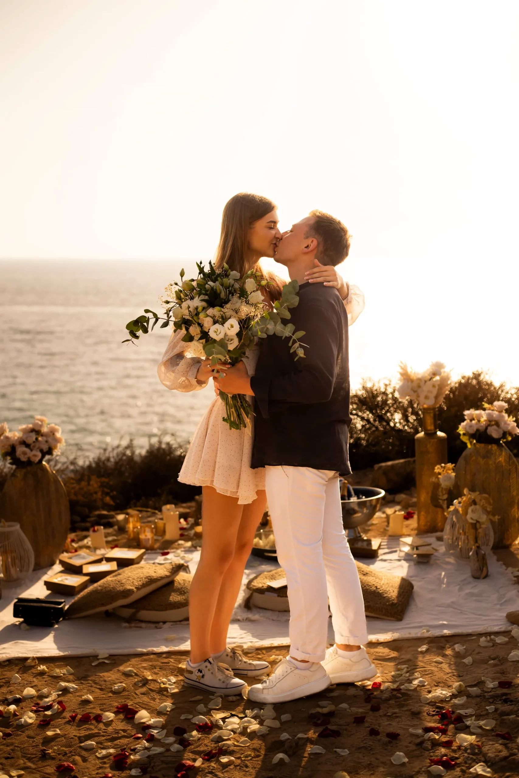 Couple kissing after a romantic proposal by the sea in Mallorca with bouquet and floral decorations