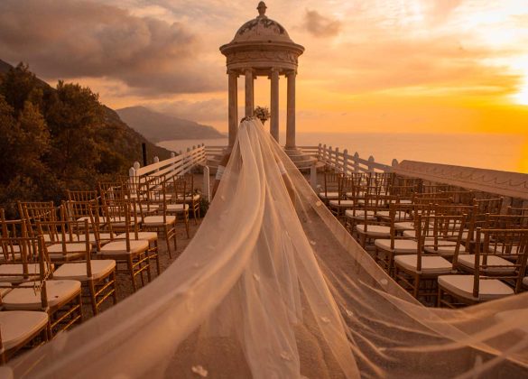 Novia con velo largo caminando hacia el templete de Son Marroig al atardecer