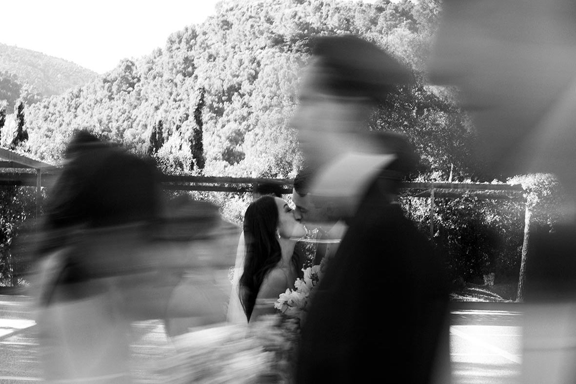 Artistic black and white photo of bride and groom kissing during luxury wedding in Mallorca, surrounded by motion blur of guests.