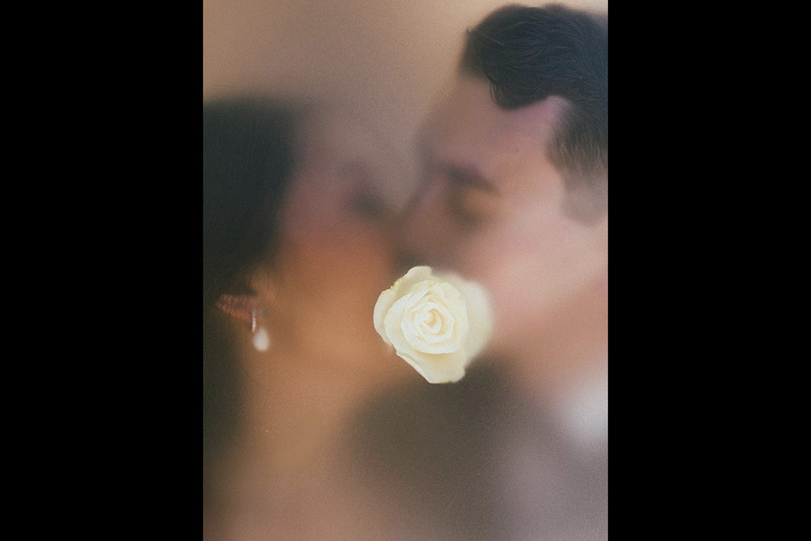 Artistic wedding photo of bride and groom kissing behind a white rose, captured by luxury wedding photographer in Mallorca.