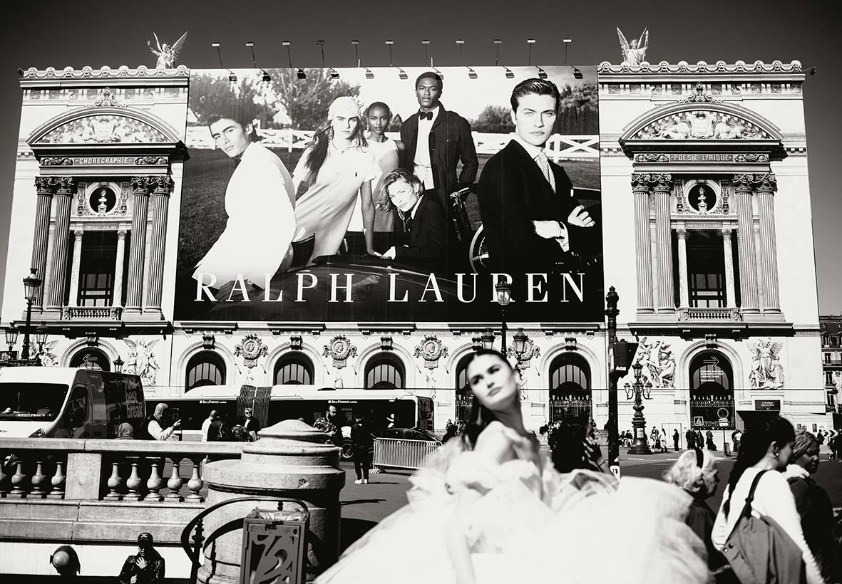 A bride in an elegant wedding dress walking in front of a giant Ralph Lauren billboard in Paris, blending high fashion with a luxurious Parisian street scene. Photo by Inma del Valle.