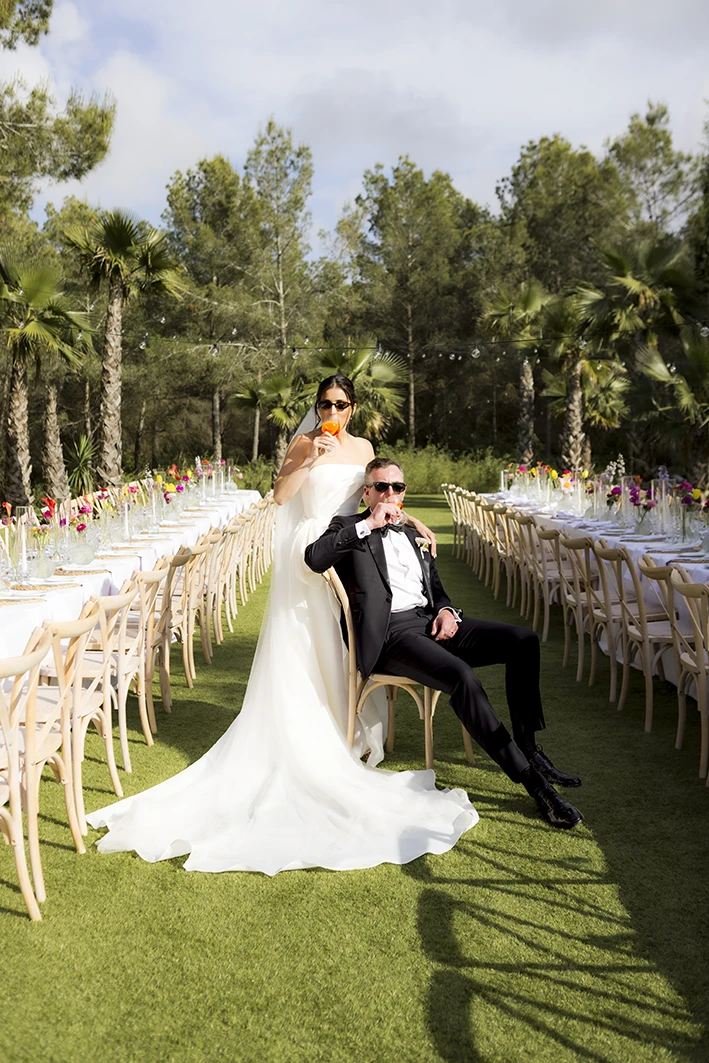 Retrato elegante de los novios sentados entre mesas al aire libre en su boda de lujo en Sitges.