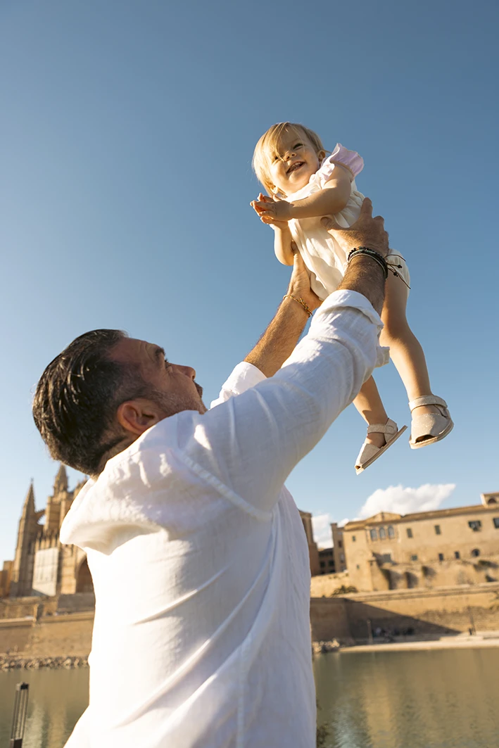 Padre levantando a su hija durante una sesión de fotografía familiar en Mallorca frente a la catedral de Palma