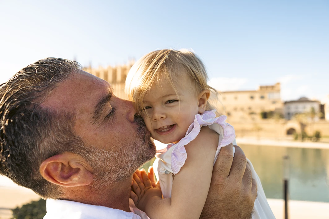 Padre besando a su hija pequeña durante una sesión de fotografía familiar en Mallorca junto al mar