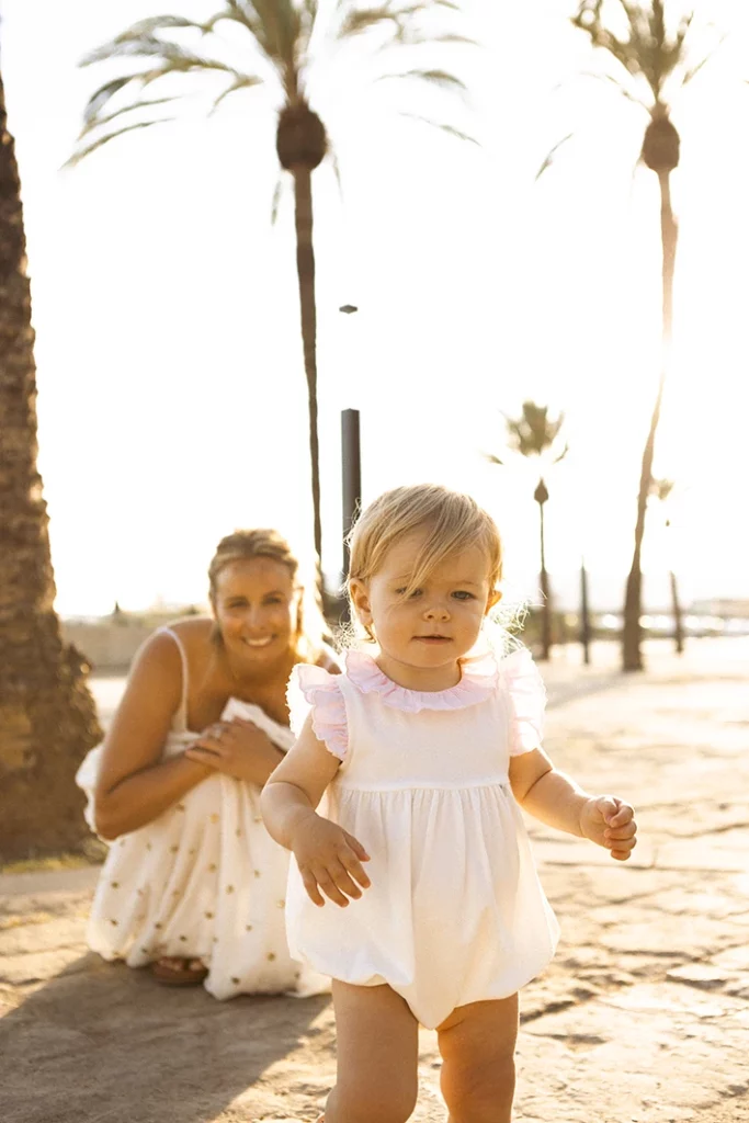 Niña caminando por la arena mientras su madre la observa durante una sesión de fotografía familiar en Mallorca