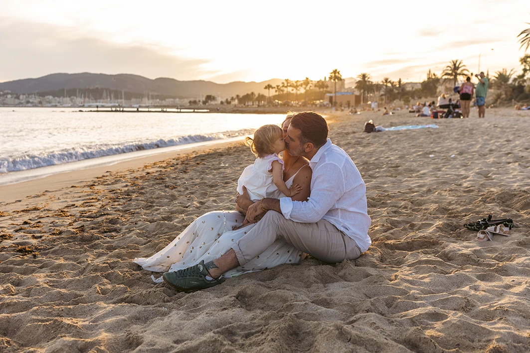 Padre abrazando a su hija en la arena al atardecer durante una sesión de fotografía familiar en Mallorca
