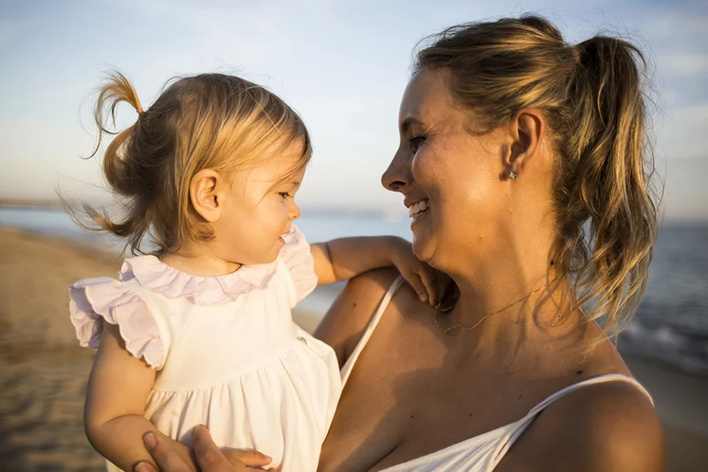 Madre sonriendo mientras sostiene a su hija durante una sesión de fotografía familiar en Mallorca