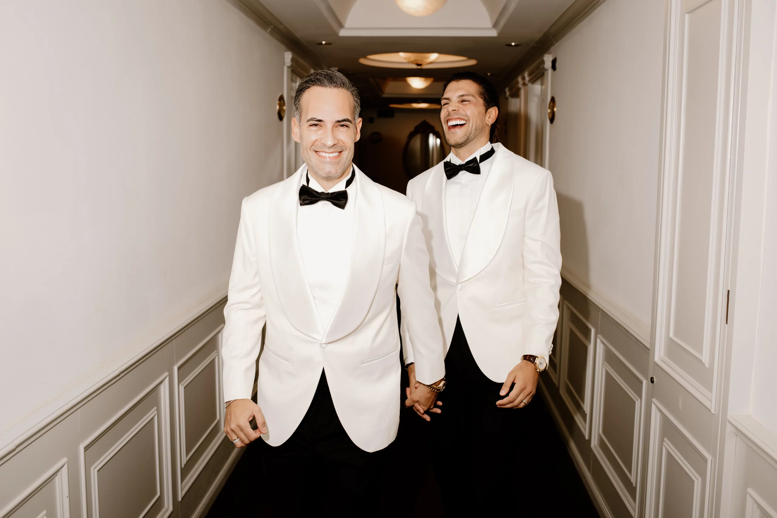 Pareja gay caminando de la mano con esmoquin blanco en su boda de lujo en Mallorca, fotografiados por Inma del Valle.