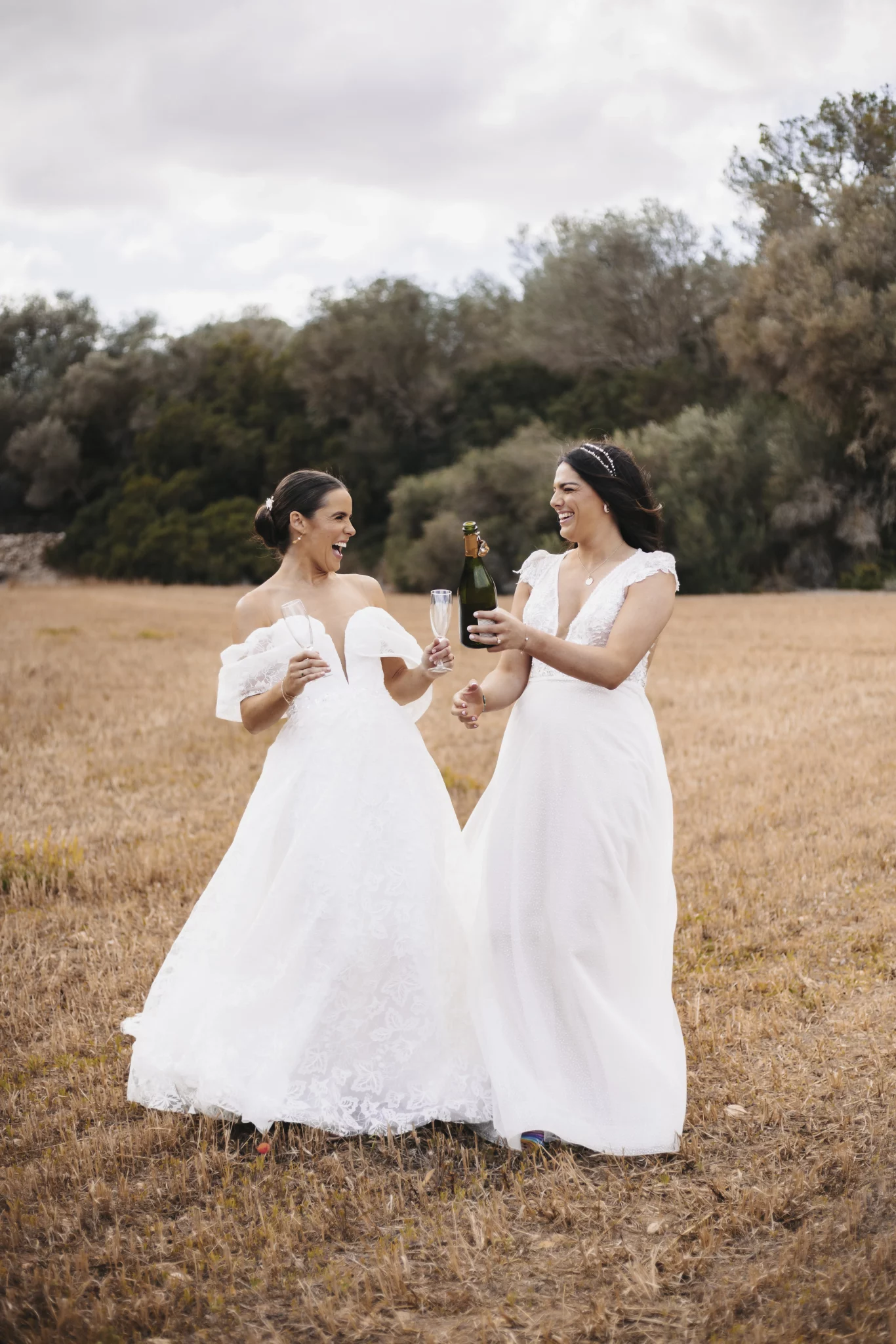 Two brides laughing and dancing in a golden field during their wedding – photo by Inma del Valle
