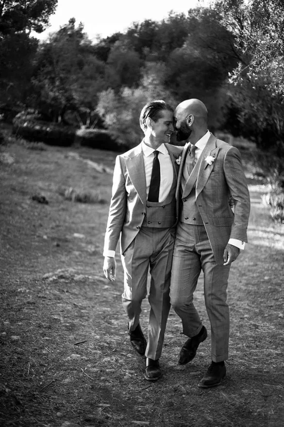 Two grooms walking arm in arm through nature – black and white photo by Inma del Valle