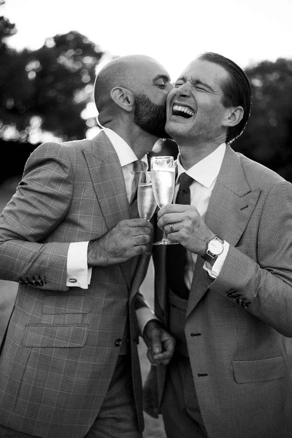 Pareja LGTB+ brindando con champán y riendo durante su boda de lujo en Mallorca, fotografiada por Inma del Valle.