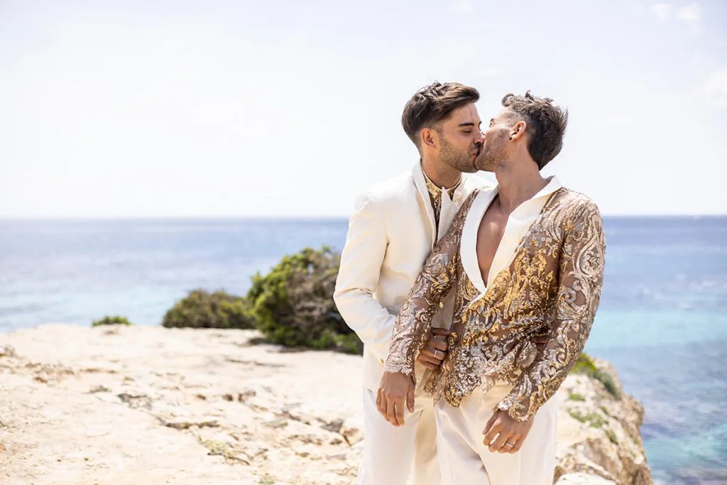 Pareja LGTB+ besándose frente al mar tras su boda de lujo en Mallorca, con vestuario elegante y estilo moderno, fotografiados por Inma del Valle.