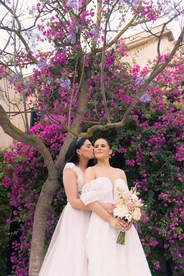 Two brides sharing a kiss in front of a blooming bougainvillea – photo by Inma del Valle