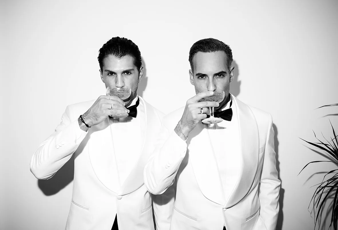 Pareja de novios con esmoquin blanco brindando durante su boda LGTB+ de lujo en Mallorca, fotografía editorial de Inma del Valle.