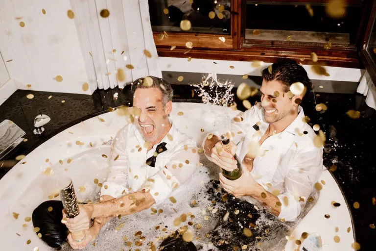 Two grooms celebrating in a bathtub with champagne and confetti – photo by Inma del Valle