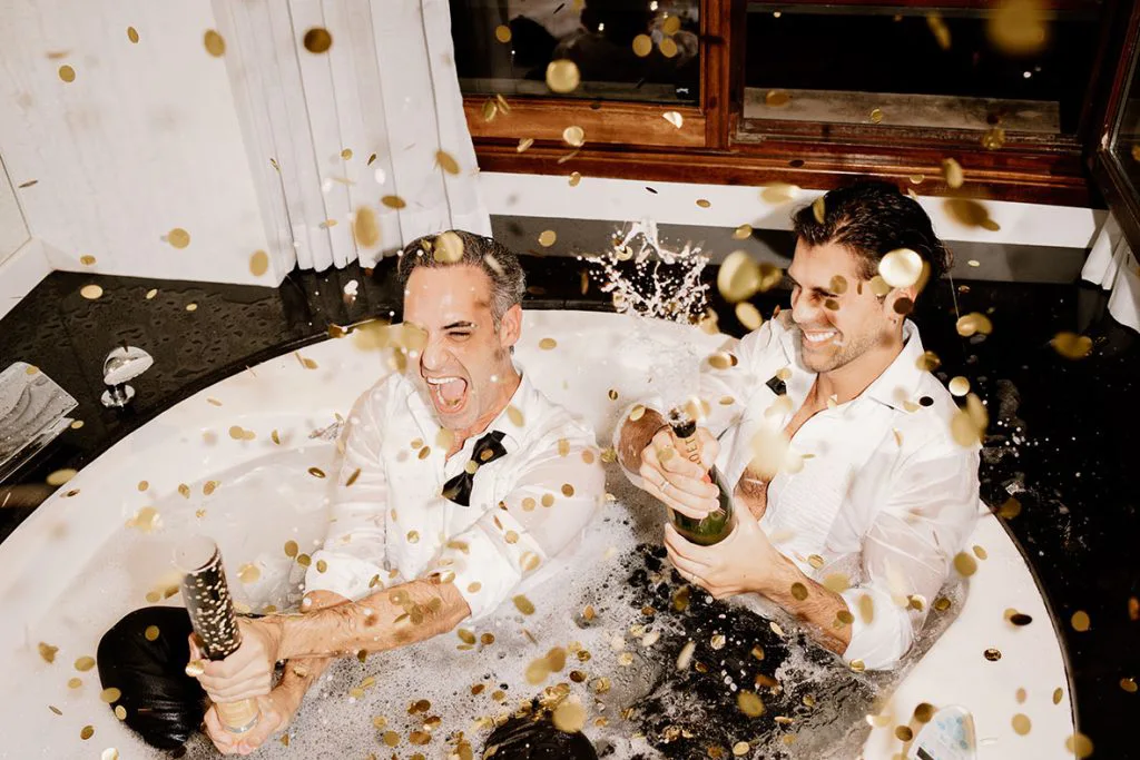Pareja gay celebrando con champán y confeti en la bañera tras su boda de lujo en Mallorca, fotografía de Inma del Valle.