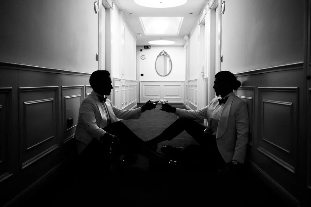 Pareja gay sentada en el pasillo de un hotel tras su boda de lujo en Mallorca, fotografía artística en blanco y negro de Inma del Valle.