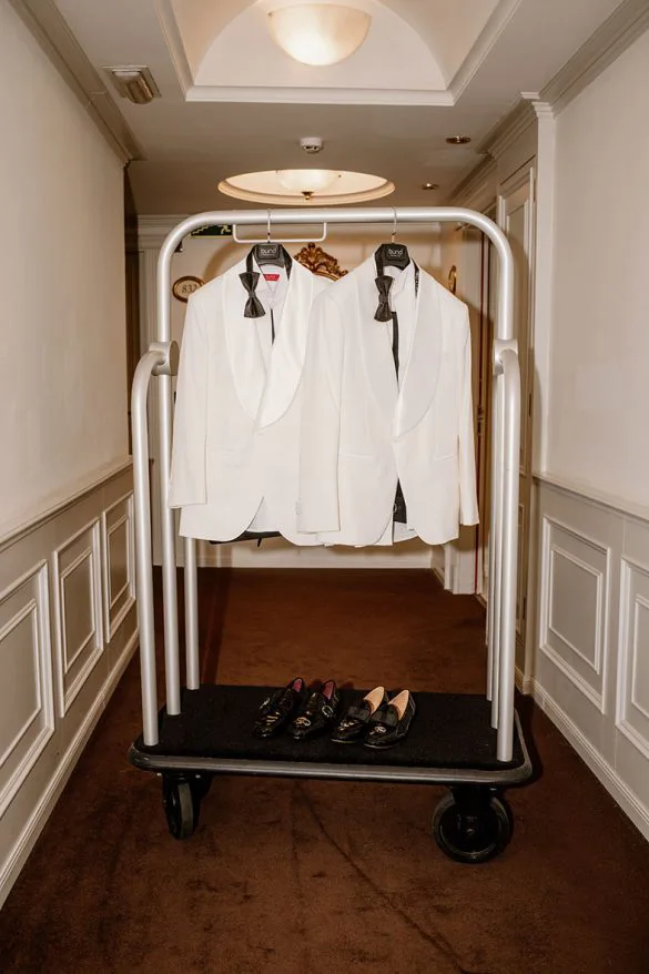 Grooms’ white tuxedos and shoes prepared on a hotel cart – photo by Inma del Valle