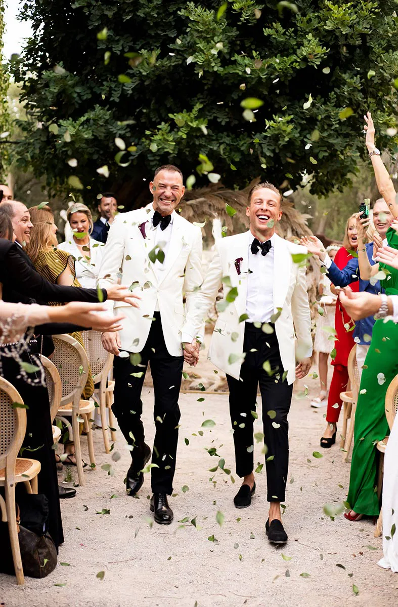 Pareja gay caminando entre pétalos tras su ceremonia de boda de lujo en Mallorca, rodeados de invitados, fotografiados por Inma del Valle.