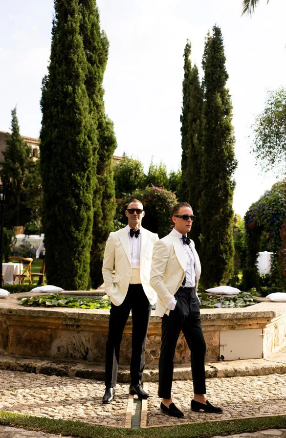 Pareja gay posando con esmoquin blanco en un jardín mediterráneo tras su boda de lujo en Mallorca, fotografía de Inma del Valle.