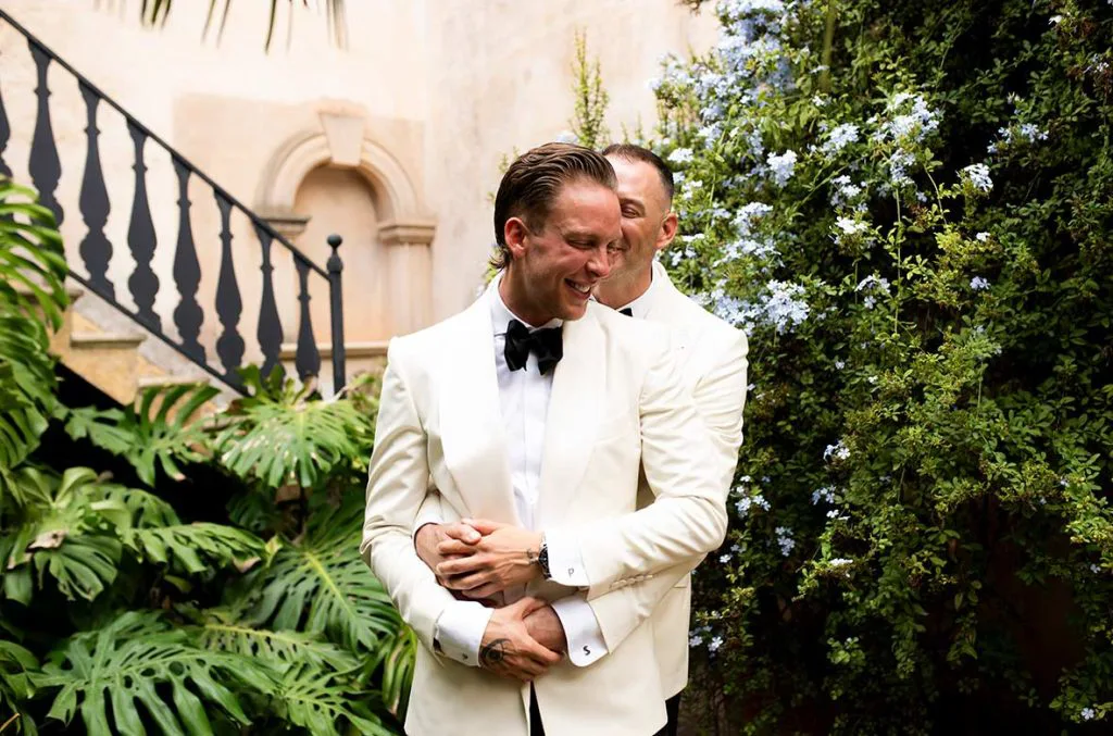 Pareja gay abrazándose entre jardines tras su boda de lujo en Mallorca, fotografía de Inma del Valle.