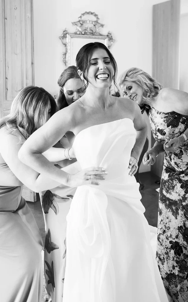 Bride laughing joyfully as her bridesmaids help her into the wedding dress in a luxury villa in Sitges.