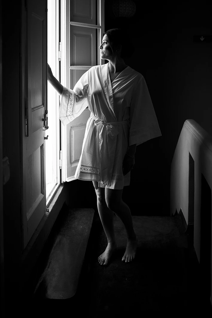 Bride in robe standing by the window before her luxury wedding in Sitges.