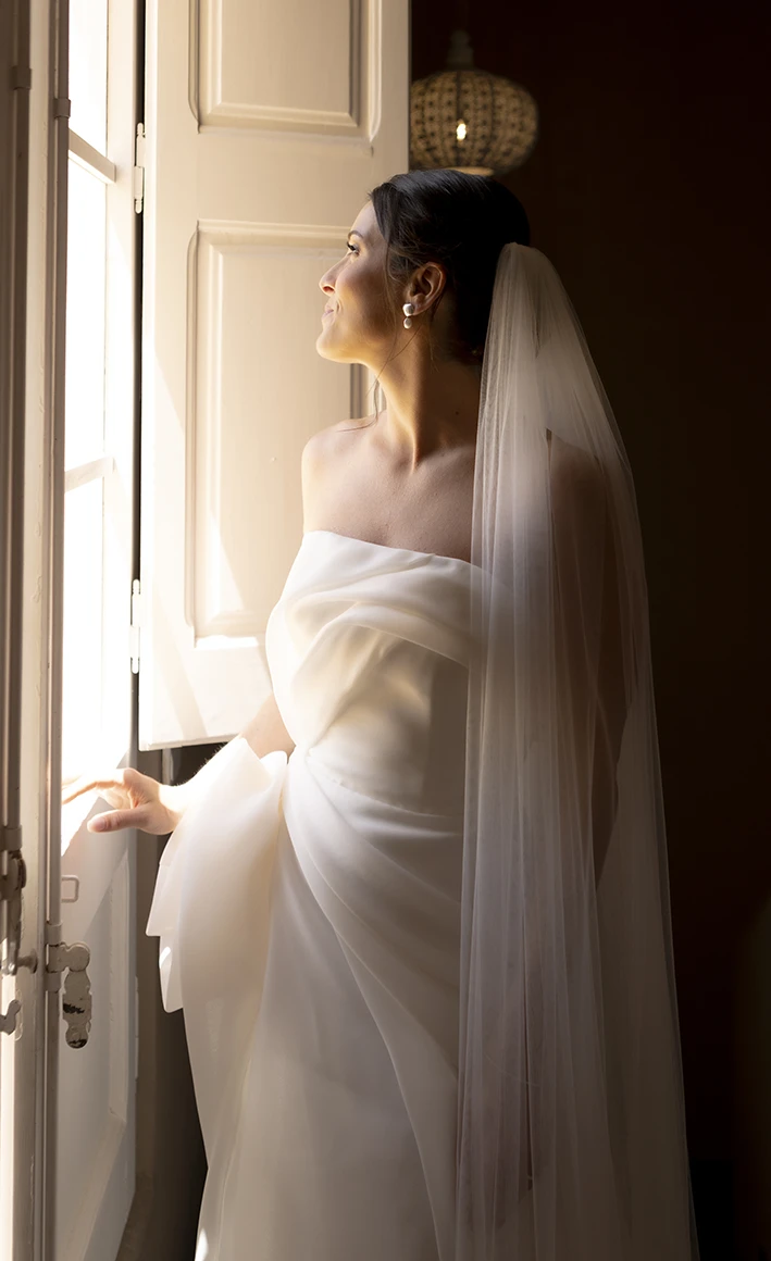 Bride gazing out the window with soft light illuminating her face and dress.