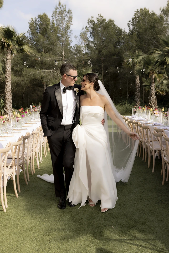 Bride and groom walk smiling through the elegant garden aisle at their luxury wedding in Sitges.