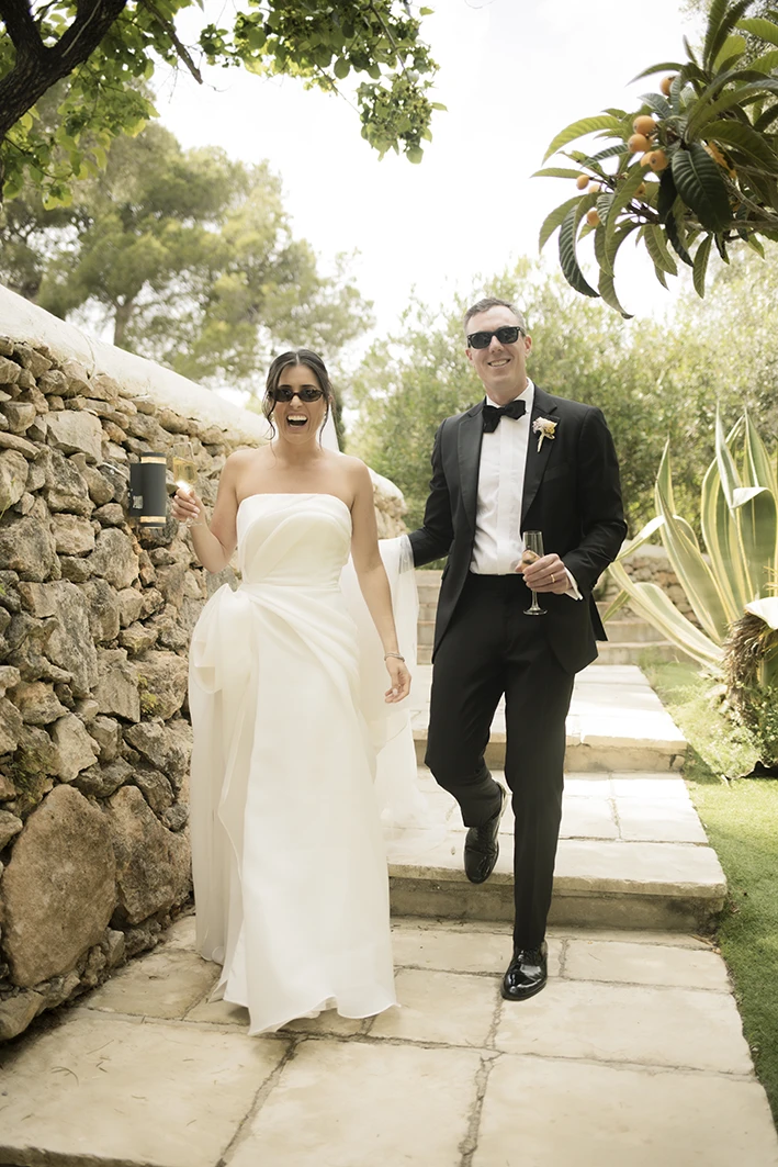 Bride and groom walking down stone steps with sunglasses at their luxury wedding in Sitges.