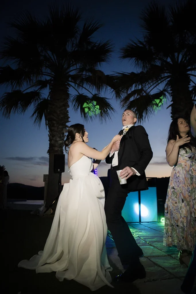 Bride and groom dancing with joy under palm trees during their luxury wedding in Sitges.