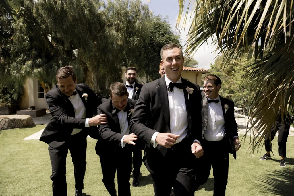 Groom and groomsmen laughing and running across a garden during a luxury wedding in Sitges.