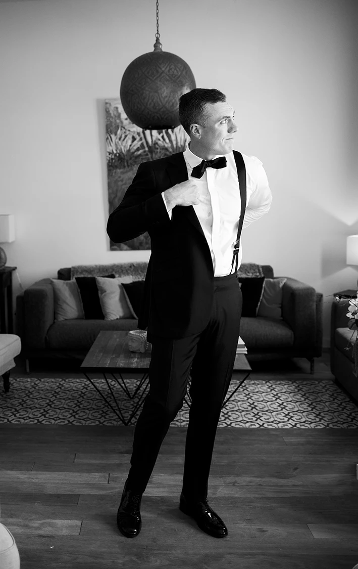 Black and white image of the groom adjusting his tuxedo suspenders before the wedding in Sitges.