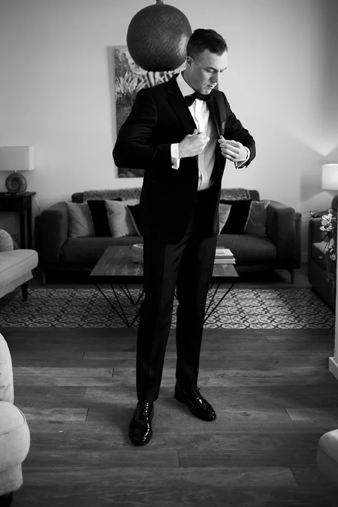 Groom adjusting his tuxedo in a living room before his wedding in Sitges, black and white image.