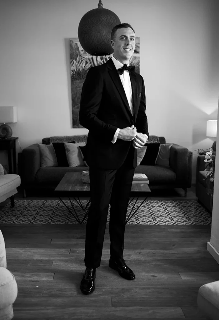Groom buttoning his suit jacket in a modern living room before the wedding in Sitges, black and white photo.