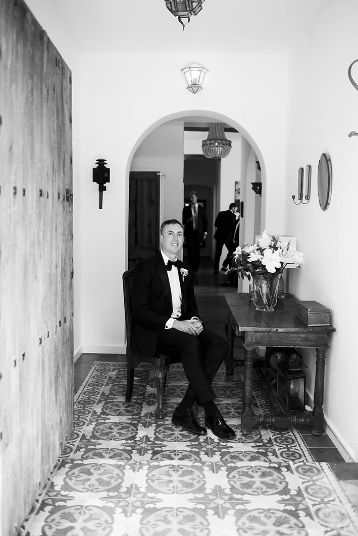 Groom sitting in a hallway before the wedding ceremony in Sitges, dressed in a tuxedo, black and white photo.