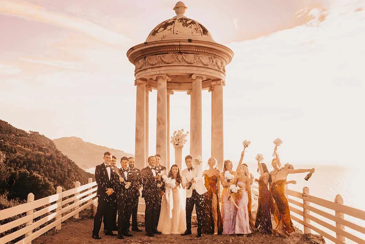 A joyful and exclusive wedding celebration at Finca Son Marroig in Mallorca, featuring the bride and groom with their bridal party, surrounded by stunning views and spraying champagne.