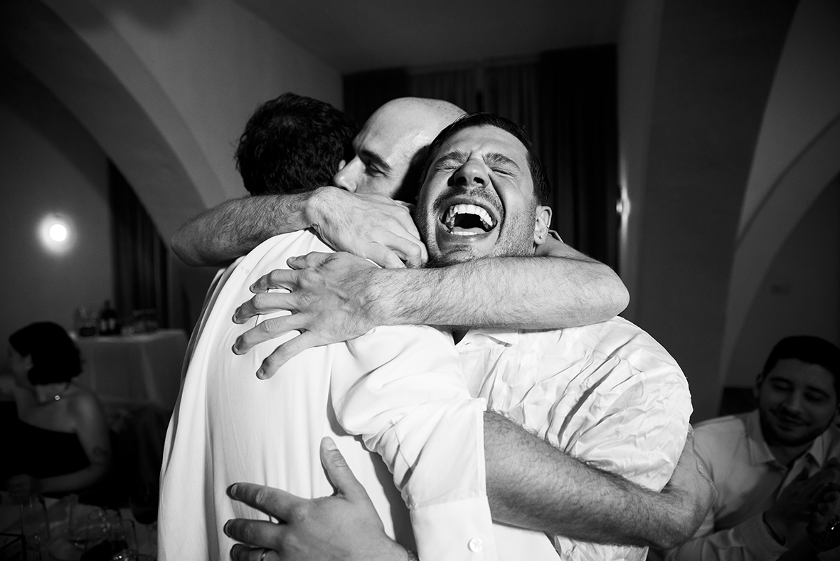 Abrazo lleno de emoción entre los novios y un invitado durante la boda de Jon y Santi en Finca Gordiola, Mallorca. Fotografía en blanco y negro de Inma del Valle.