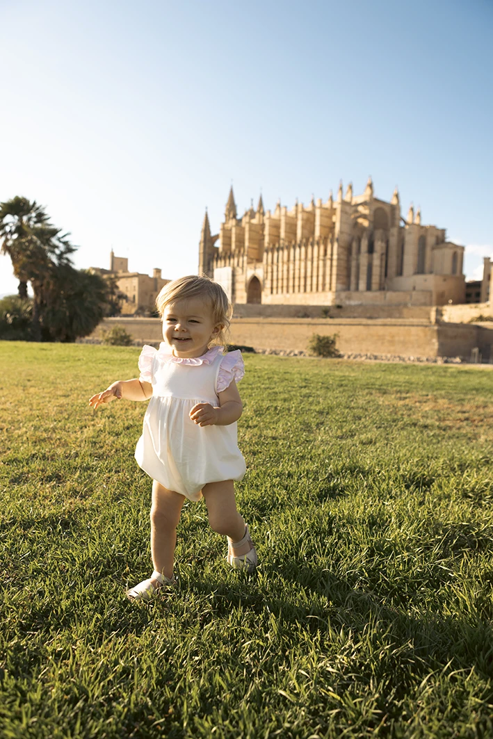 Smiling toddler walking on the grass at Parc de la Mar with La Seu Cathedral in the background, Palma de Mallorca.