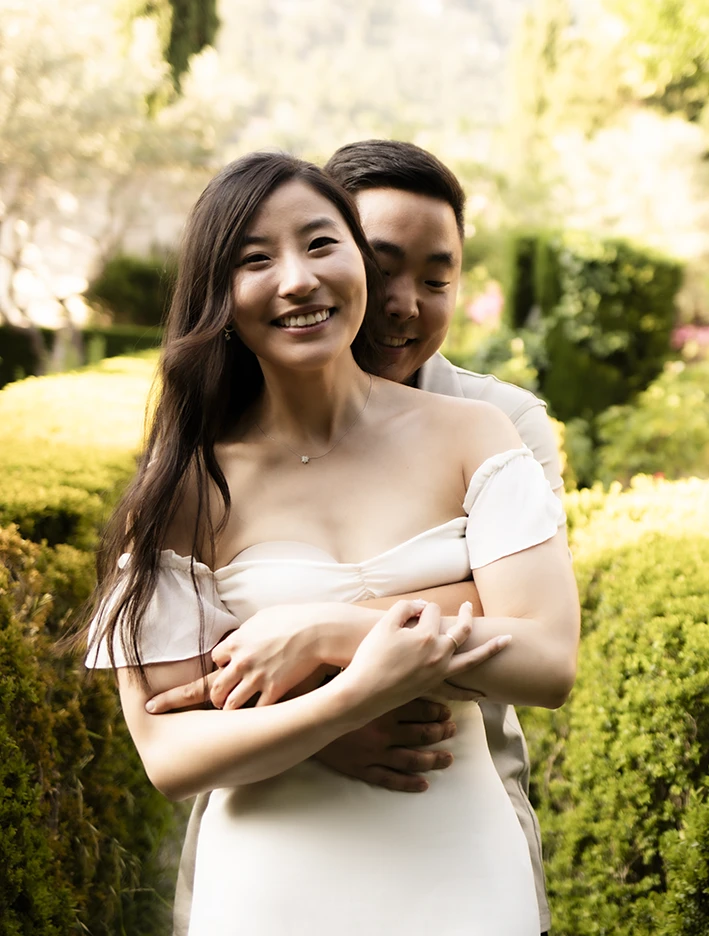 Mathew hugs Emily as they smile in a romantic garden during their proposal in Mallorca.