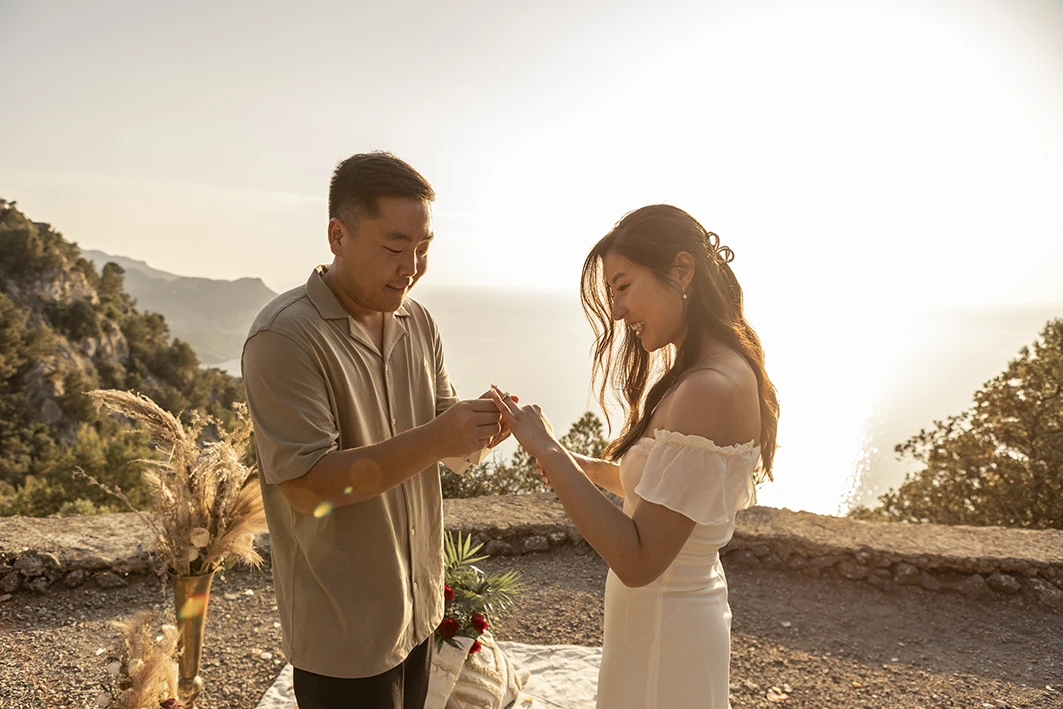 Groom placing engagement ring on bride's finger during Mallorca proposal.
