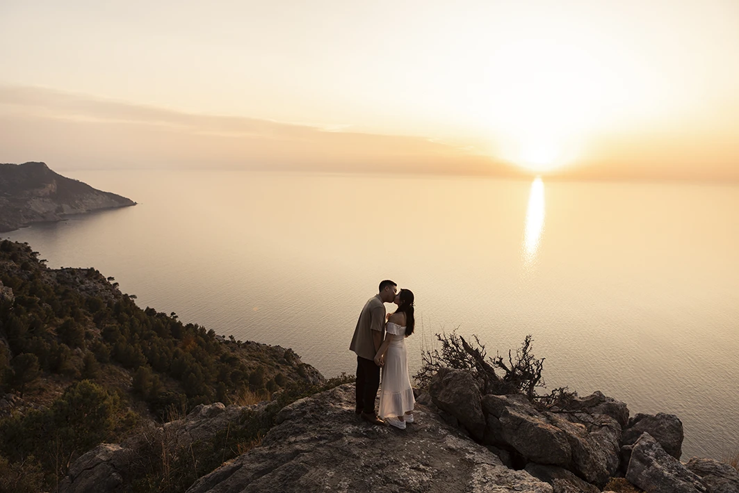 Couple kissing on a cliff at sunset after their wedding proposal in Mallorca.