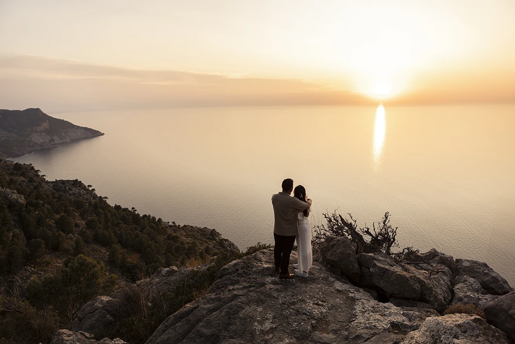 Embracing couple on a cliff during their wedding proposal in Mallorca at sunset.