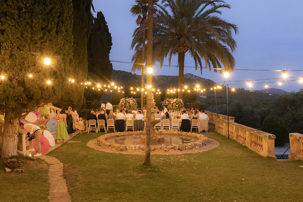 Cena al aire libre iluminada con guirnaldas de luces en el jardín de Son Togores durante la boda.