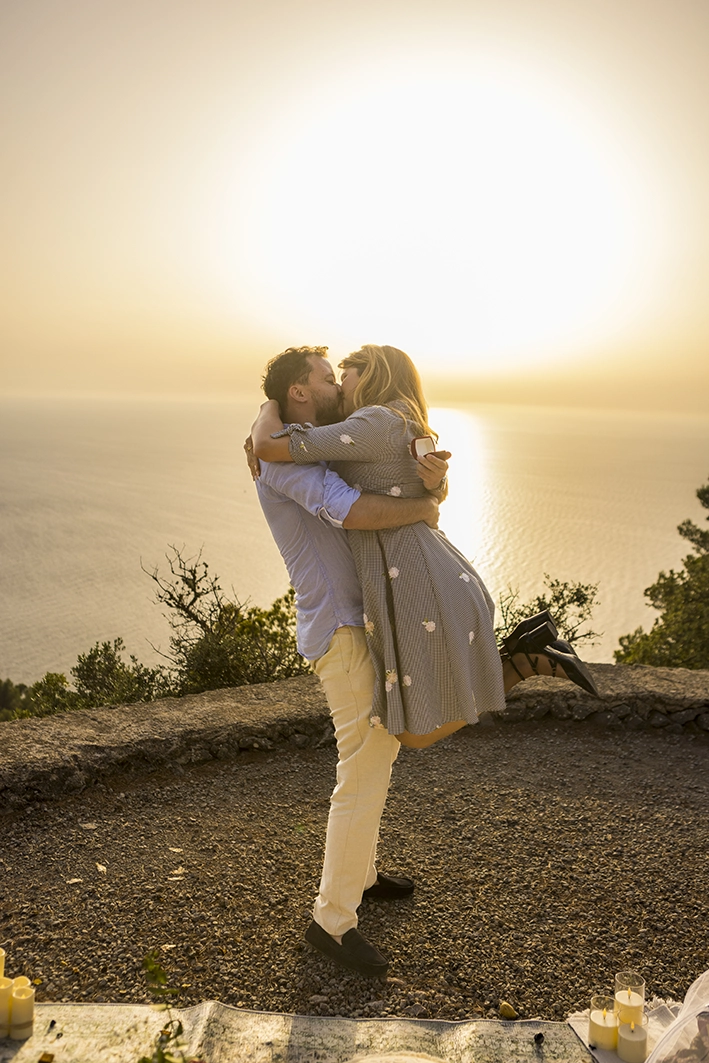 Couple embracing after a surprise marriage proposal at sunset on a Mallorca cliff.