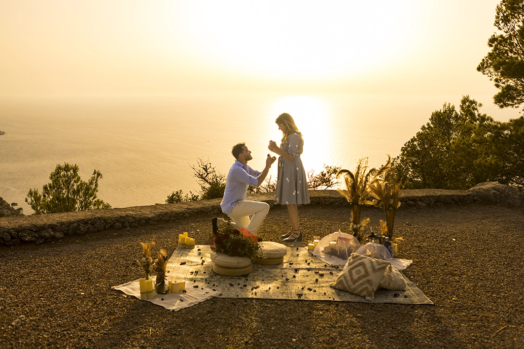 Romantic sunset proposal on a Mallorca cliff with styled picnic and the couple in the “yes” moment.
