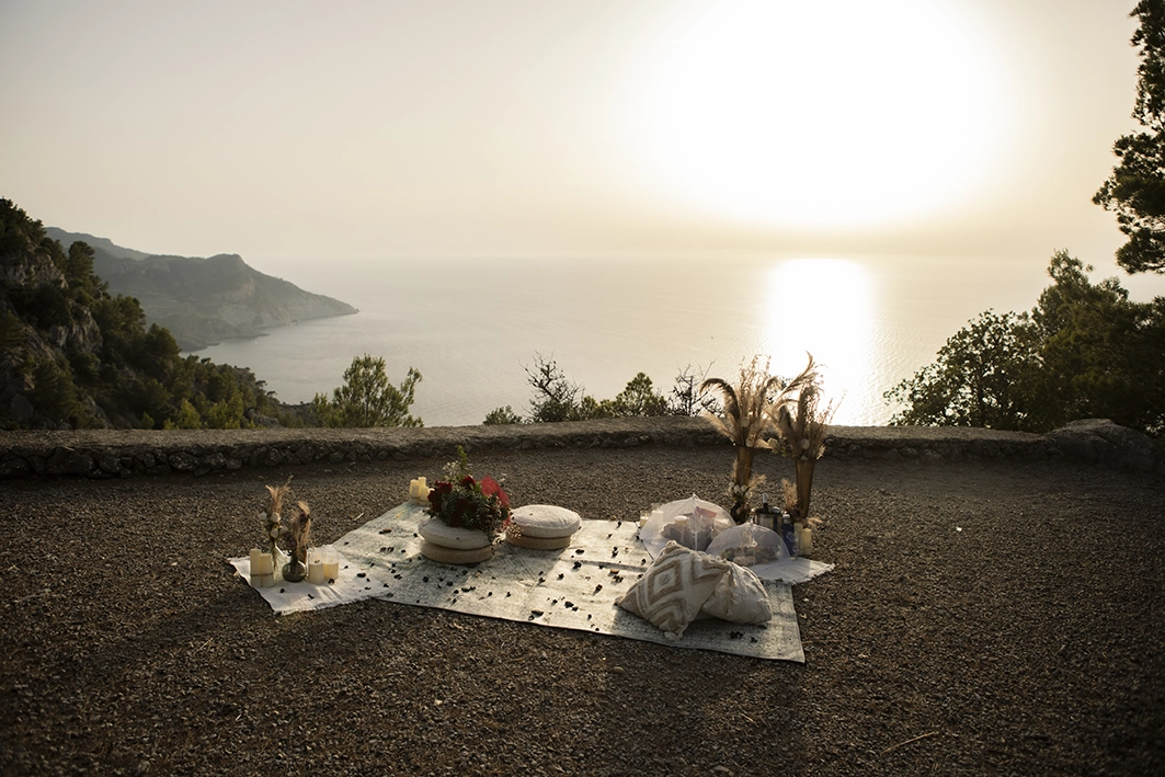 Romantic picnic setup at sunset on a Mallorca cliff, prepared for a surprise marriage proposal.