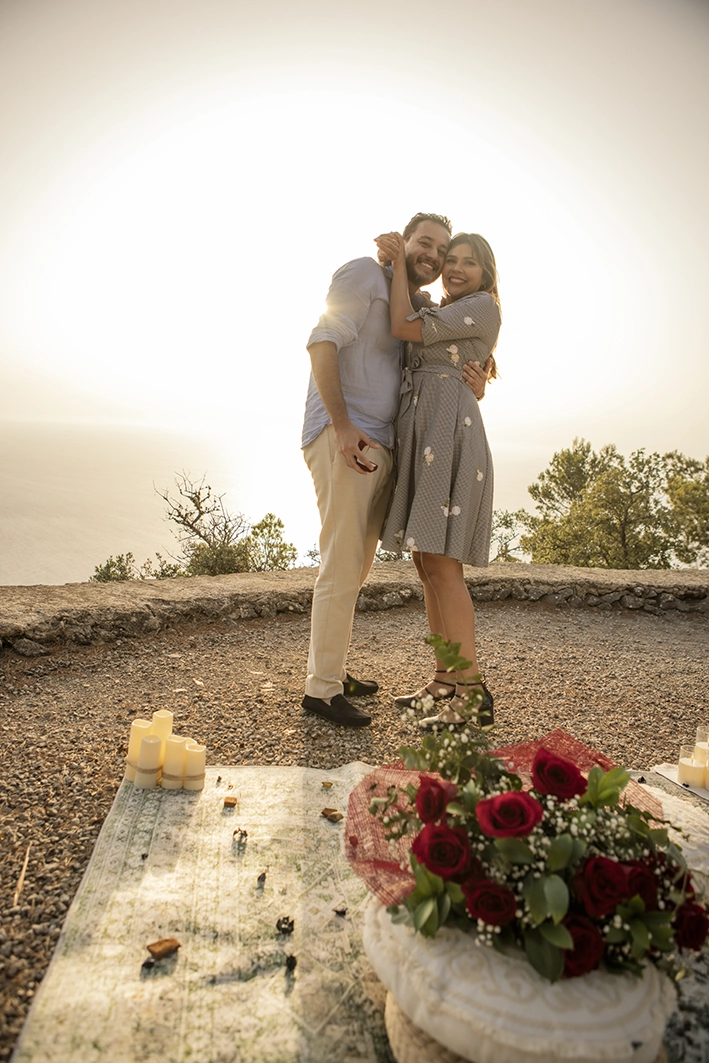 Happy couple embracing after the proposal, beside a beautifully styled picnic on a Mallorca cliff.