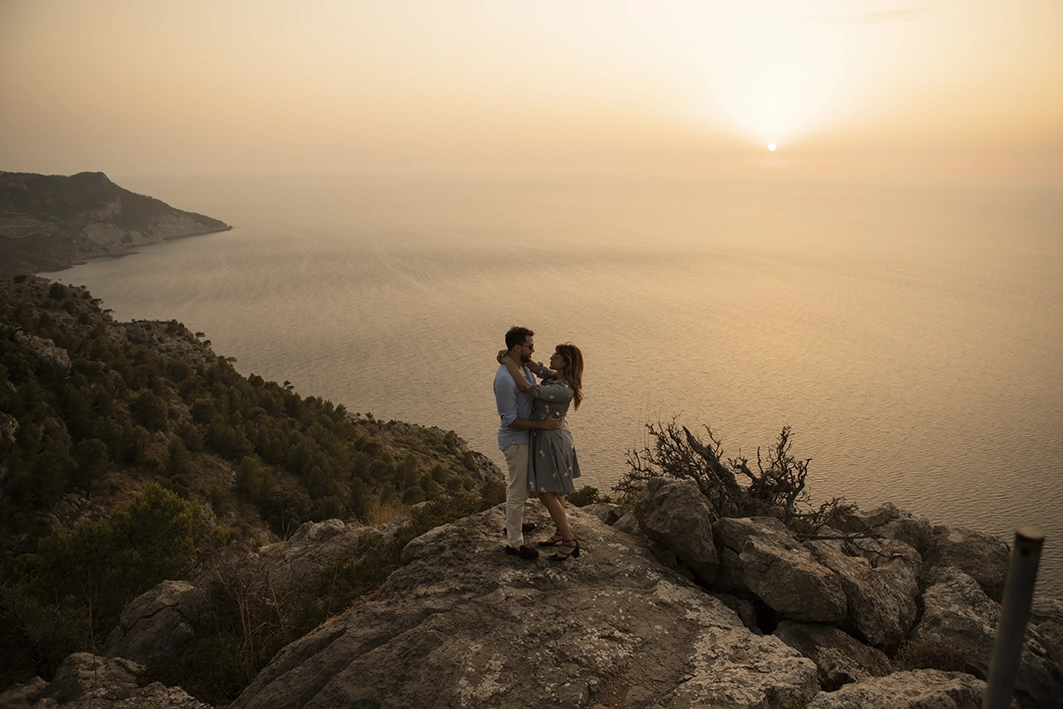 Couple embracing on a cliff in Mallorca with the sunset in the background after their proposal.